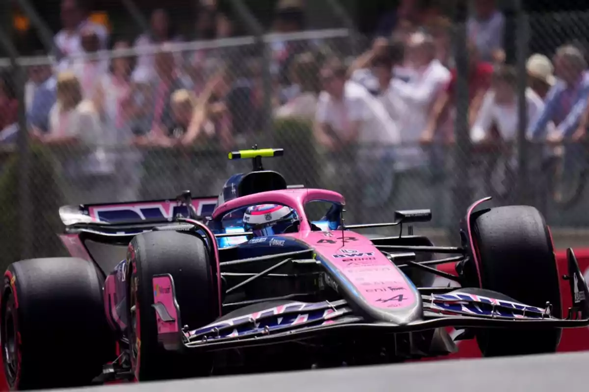 Pink and blue Formula 1 car on a racetrack with spectators in the background Pink and blue Formula 1 car on a racetrack with spectators in the background