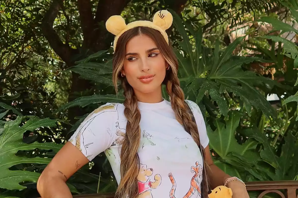 Mujer con diadema de orejas amarillas y camiseta de Winnie the Pooh posando frente a plantas verdes