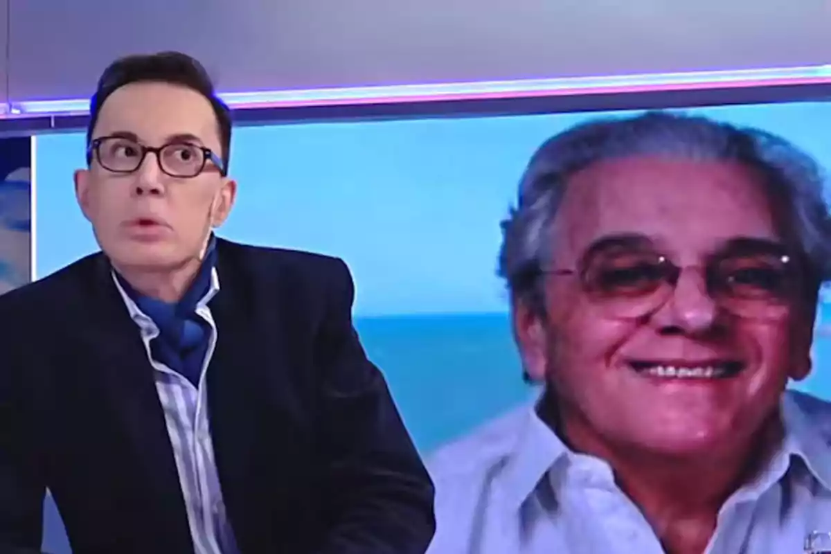 Un hombre con gafas y un pañuelo azul está sentado frente a una pantalla que muestra a otro hombre mayor sonriendo. Un hombre con gafas y un pañuelo azul está sentado frente a una pantalla que muestra a otro hombre mayor sonriendo.