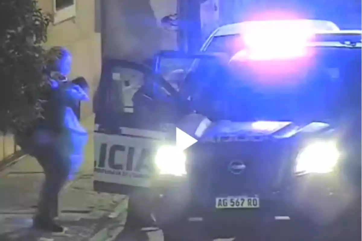 Patrulla policial con las luces encendidas y una persona de pie junto a la puerta del vehículo en una calle de noche
