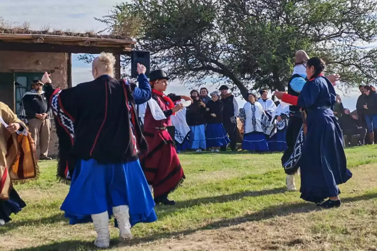 Personas vestidas con trajes tradicionales bailan al aire libre en un entorno rural.