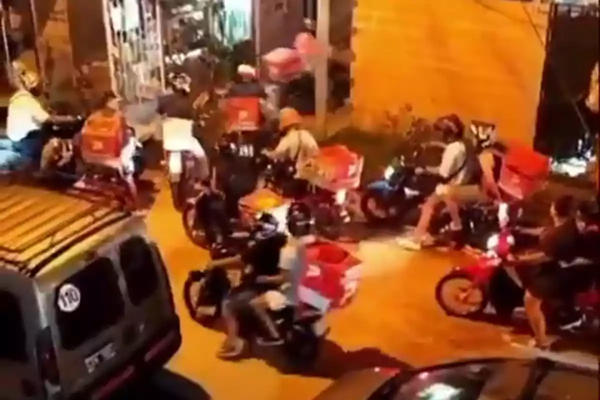 Un grupo de motociclistas con cajas de reparto se reúne en una calle iluminada por la noche.