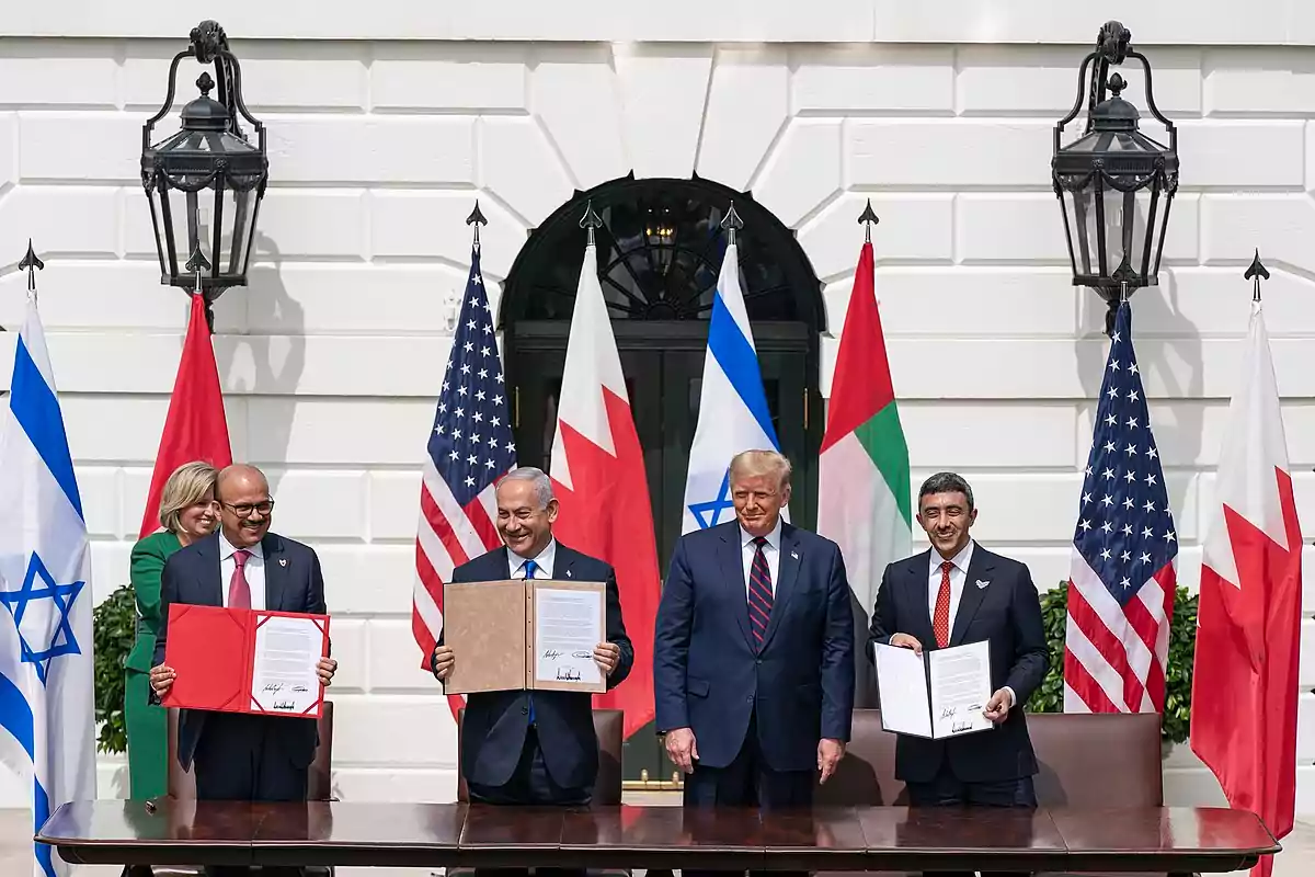 Cinco personas posan frente a banderas de Israel, Estados Unidos, Baréin y Emiratos Árabes Unidos, sosteniendo documentos en un evento oficial.