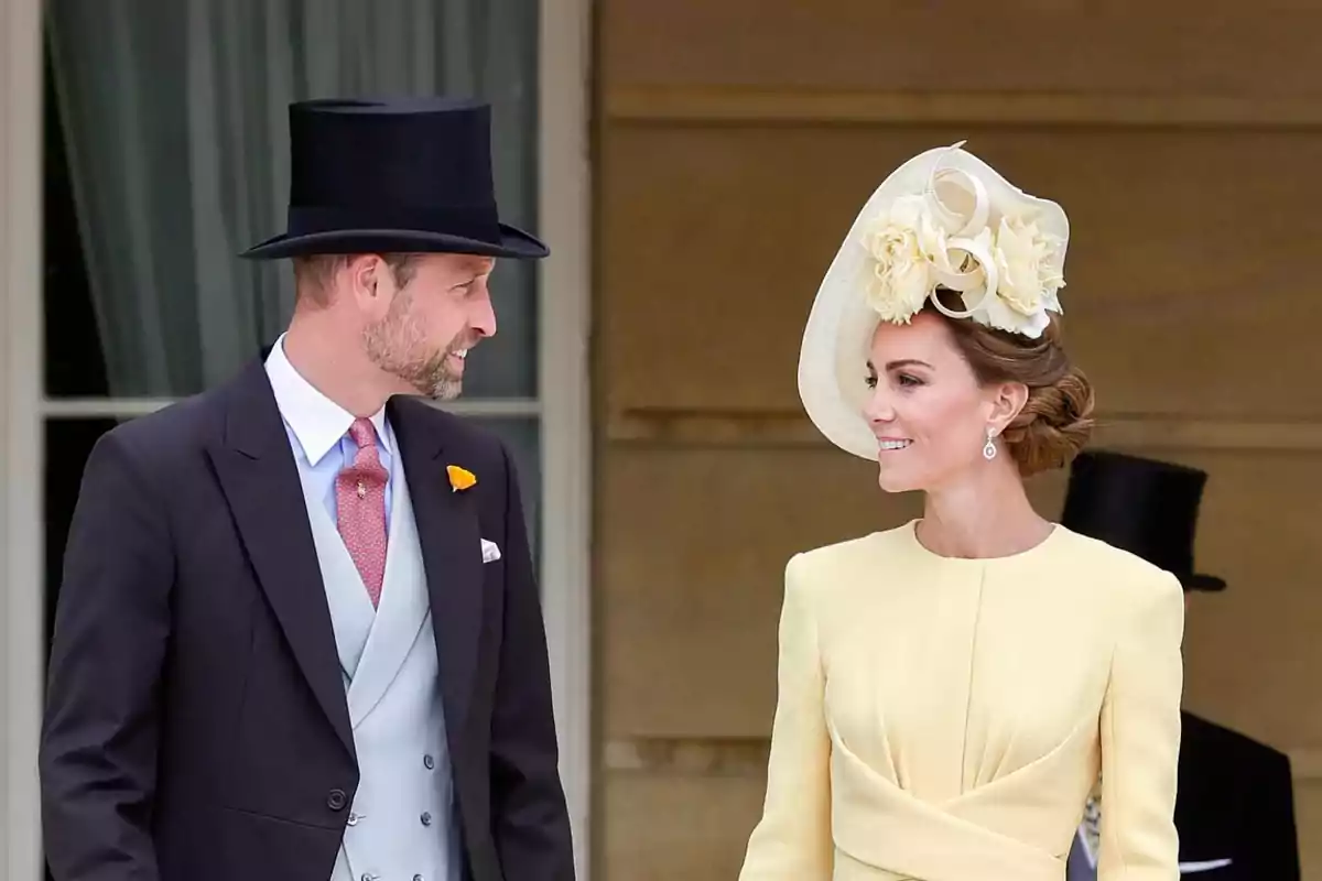 Un hombre con sombrero de copa y una mujer con un elegante vestido amarillo y tocado floral conversan sonrientes en un evento formal al aire libre.