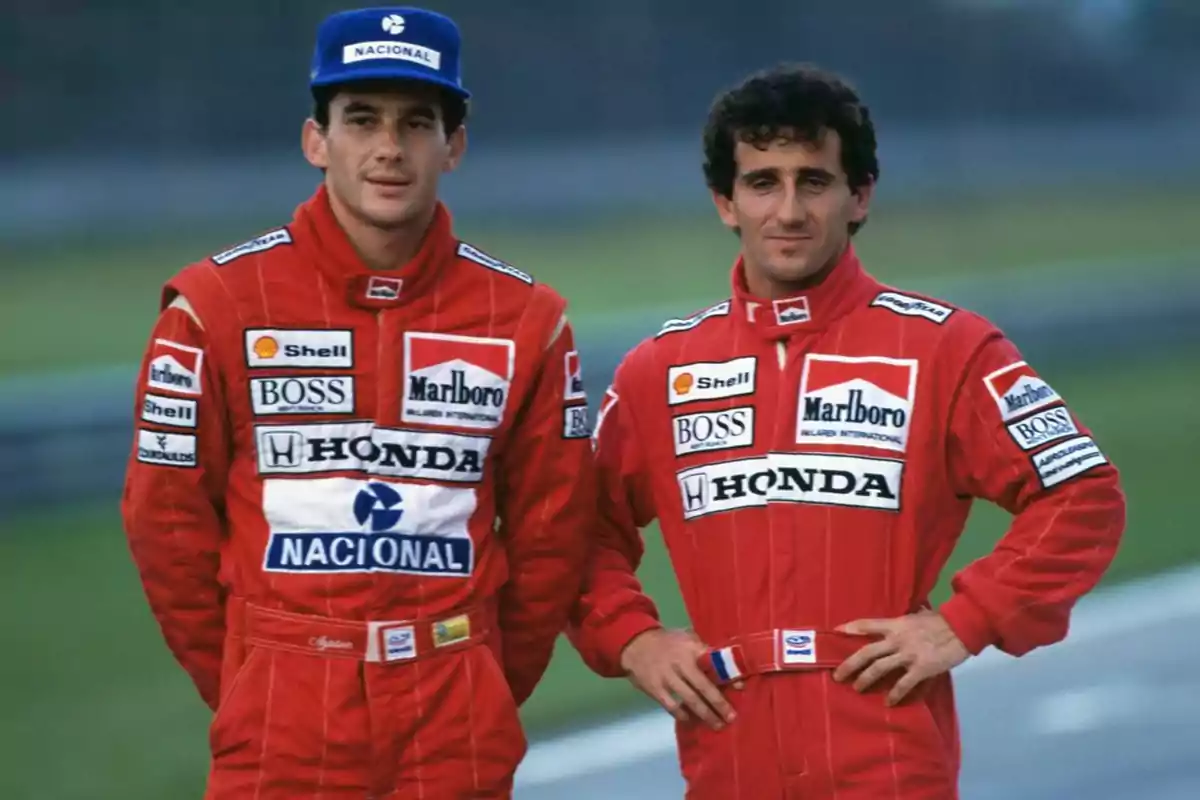 Two racing drivers in red racing suits with sponsor logos pose together on a track. Two racing drivers in red racing suits with sponsor logos pose together on a track.