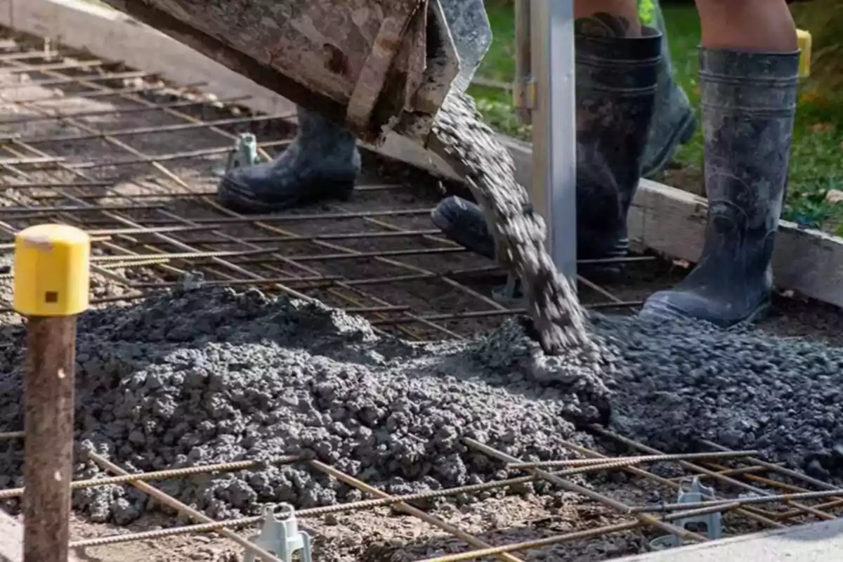 Una persona con botas de goma vierte concreto con restos de café sobre una estructura de varillas de metal en una obra de construcción. Una persona con botas de goma vierte concreto con restos de café sobre una estructura de varillas de metal en una obra de construcción.