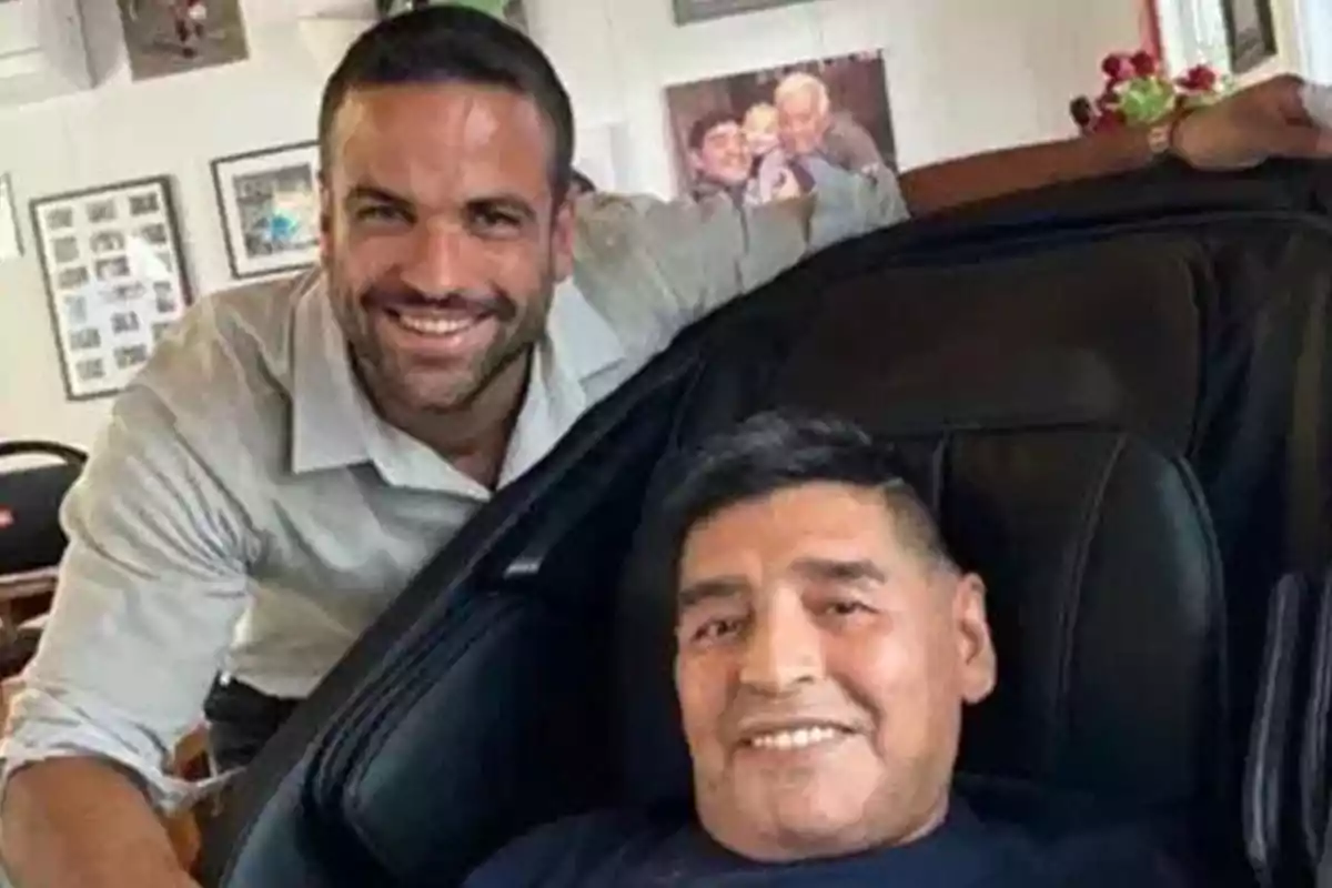 Dos personas sonríen mientras posan para una foto en un ambiente interior con cuadros en la pared. Dos personas sonríen mientras posan para una foto en un ambiente interior con cuadros en la pared.