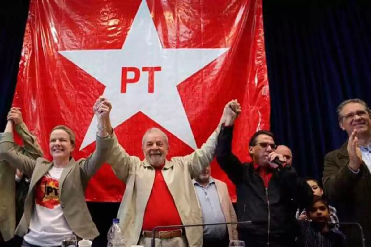 Un grupo de personas levanta las manos frente a una gran bandera roja con una estrella blanca y las letras PT.