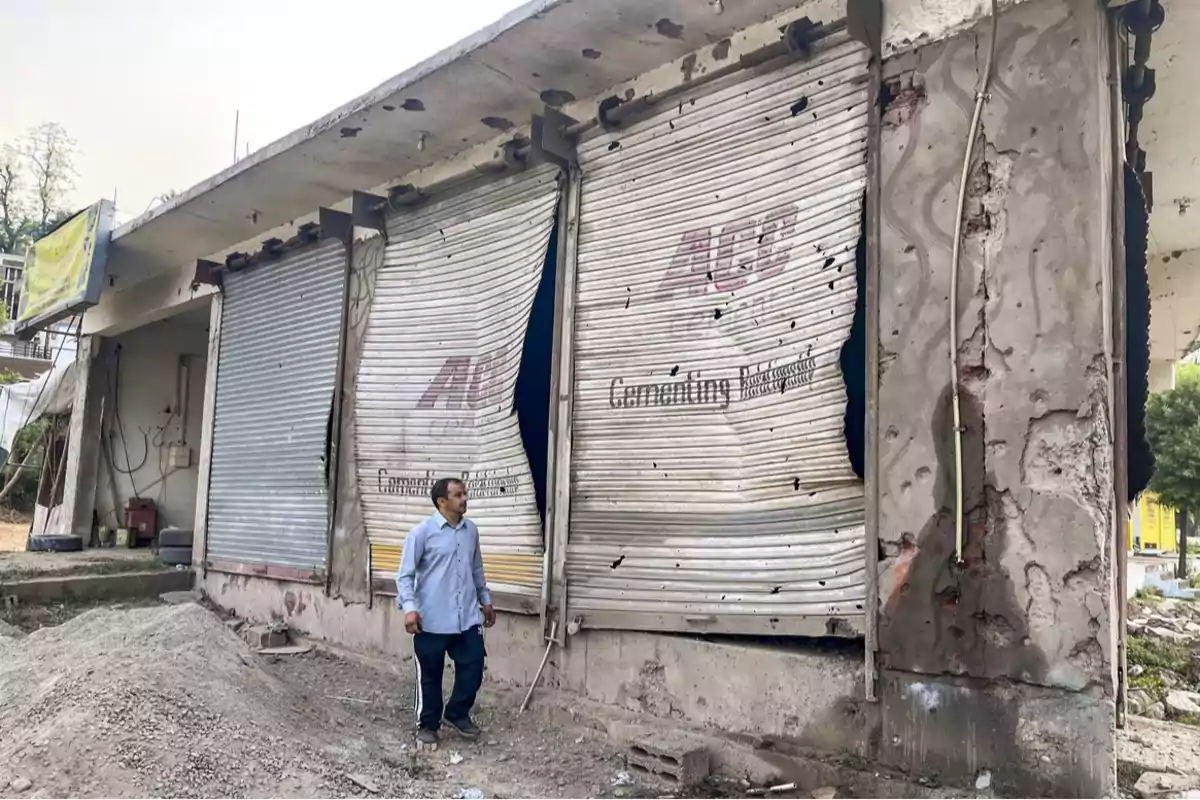 A man observes a building with damaged metal shutters and deteriorated walls.