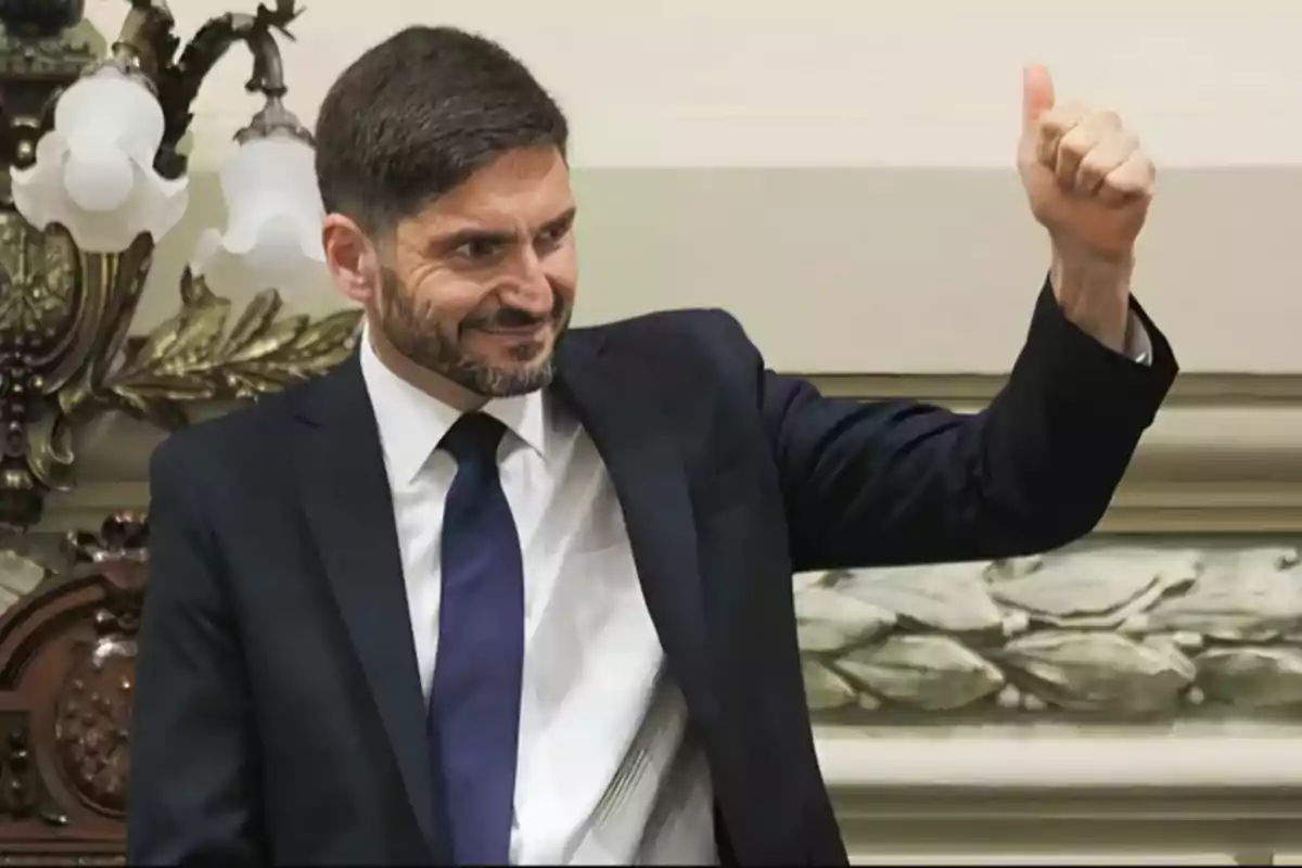 Hombre con traje oscuro y corbata azul levantando el pulgar en señal de aprobación.