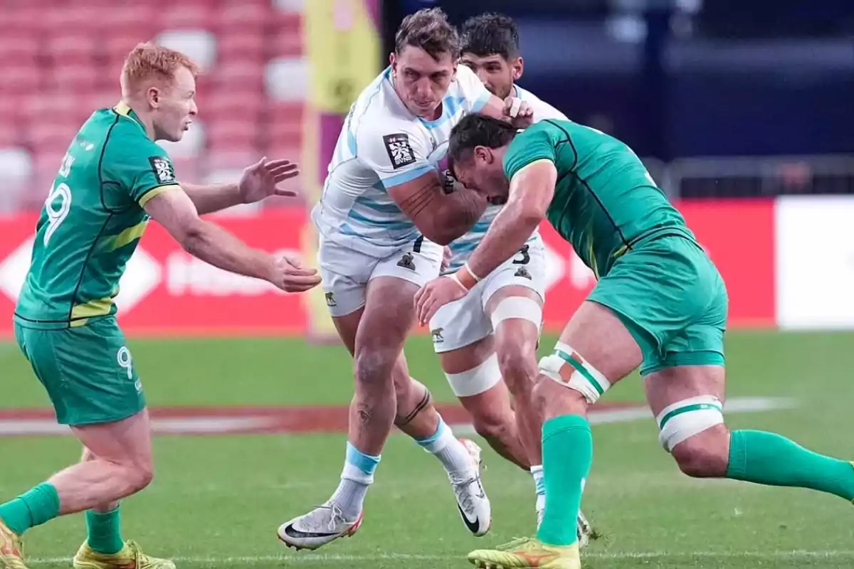 Jugadores de rugby en acción durante un partido, uno de ellos intenta avanzar mientras es bloqueado por oponentes.