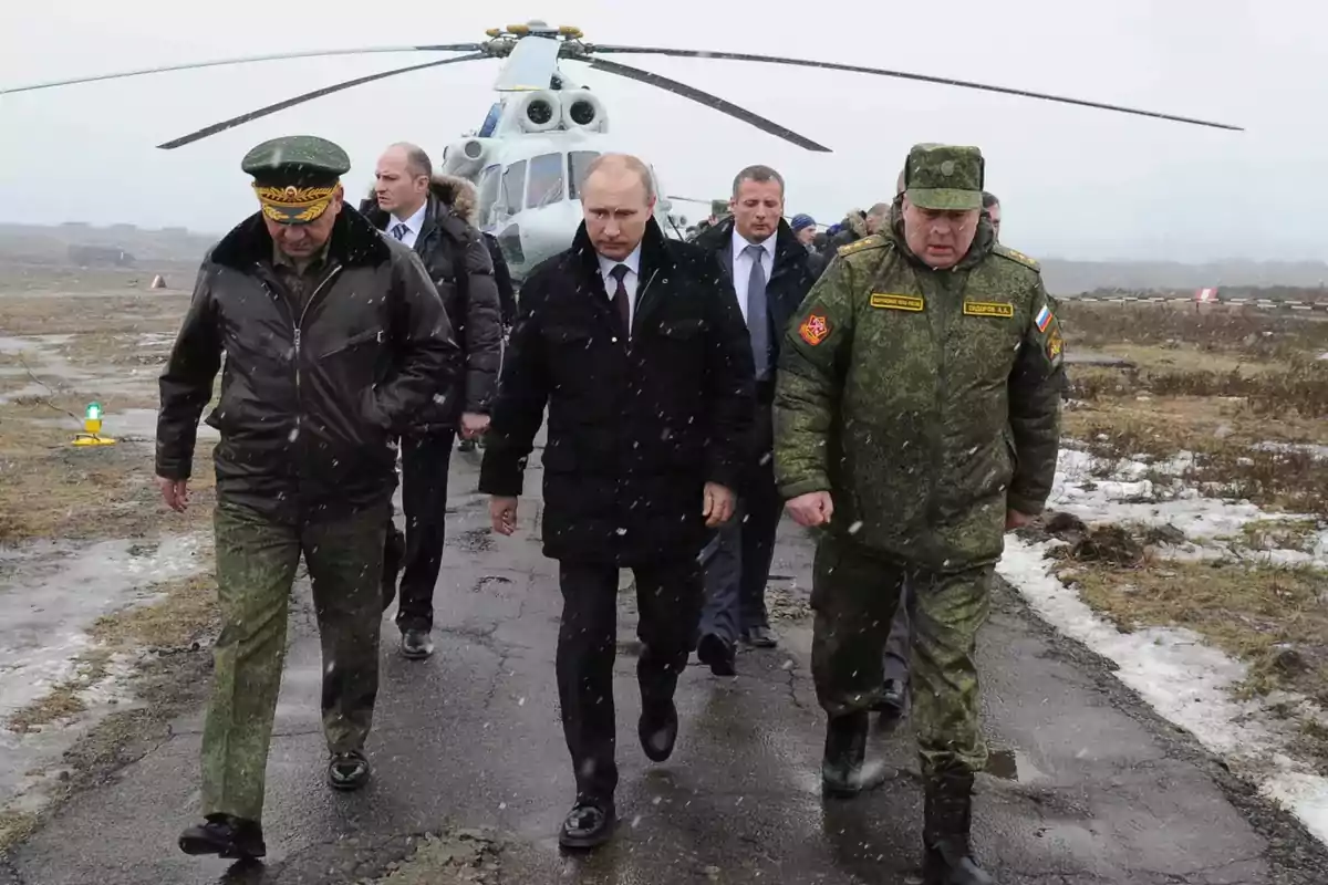 A group of men in coats and military uniforms walks along a snowy runway with a helicopter in the background. A group of men in coats and military uniforms walks along a snowy runway with a helicopter in the background.