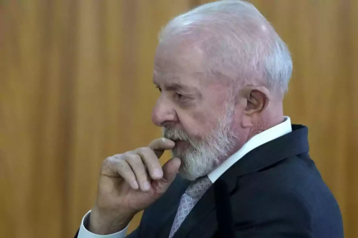 An older man with a white beard and a dark suit is thoughtful with his hand on his chin.