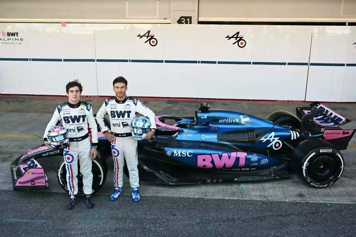 Dos pilotos con sus cascos posan junto a un auto de Fórmula 1 del equipo Alpine decorado en azul y rosa en el pit lane Dos pilotos con sus cascos posan junto a un auto de Fórmula 1 del equipo Alpine decorado en azul y rosa en el pit lane
