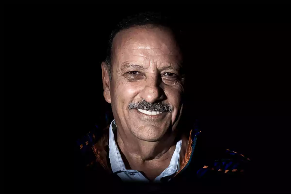 Retrato de un hombre mayor sonriendo con fondo negro.