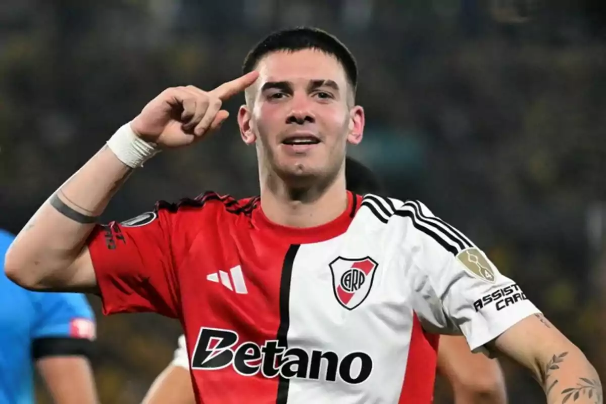 Un jugador de fútbol con la camiseta de River Plate celebra un gol señalando su cabeza con el dedo índice. Un jugador de fútbol con la camiseta de River Plate celebra un gol señalando su cabeza con el dedo índice.