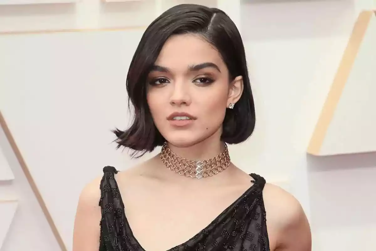 Mujer joven de cabello corto y oscuro con vestido negro elegante y collar dorado posando en una alfombra roja Mujer joven de cabello corto y oscuro con vestido negro elegante y collar dorado posando en una alfombra roja