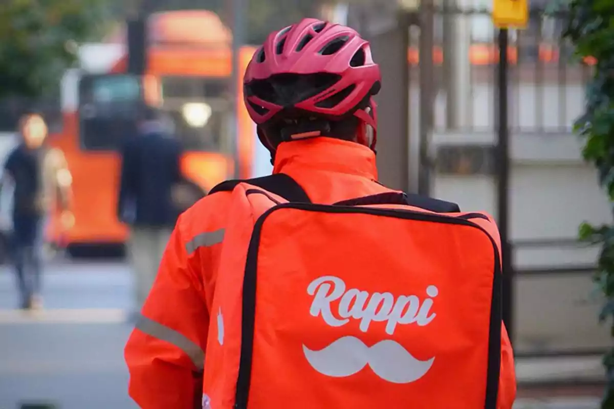 Repartidor de Rappi con mochila y casco rosa en la calle.