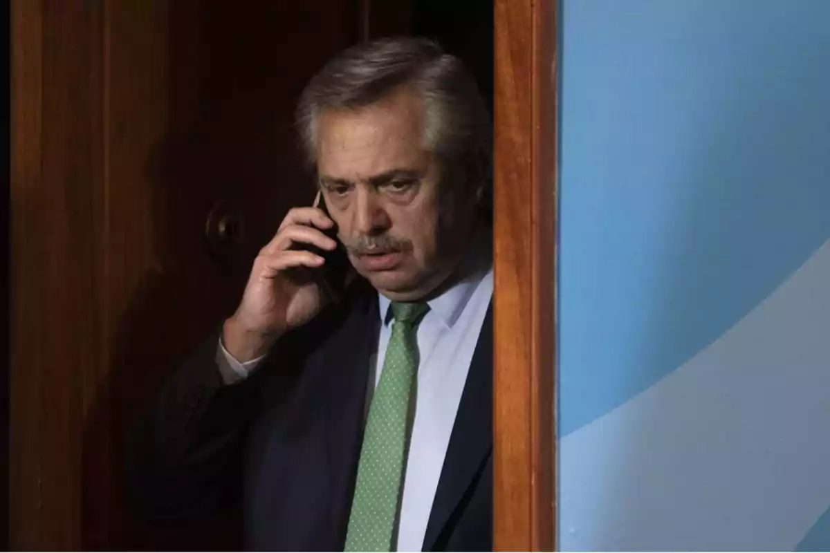 Hombre de traje con corbata verde hablando por teléfono móvil mientras se encuentra en el umbral de una puerta.