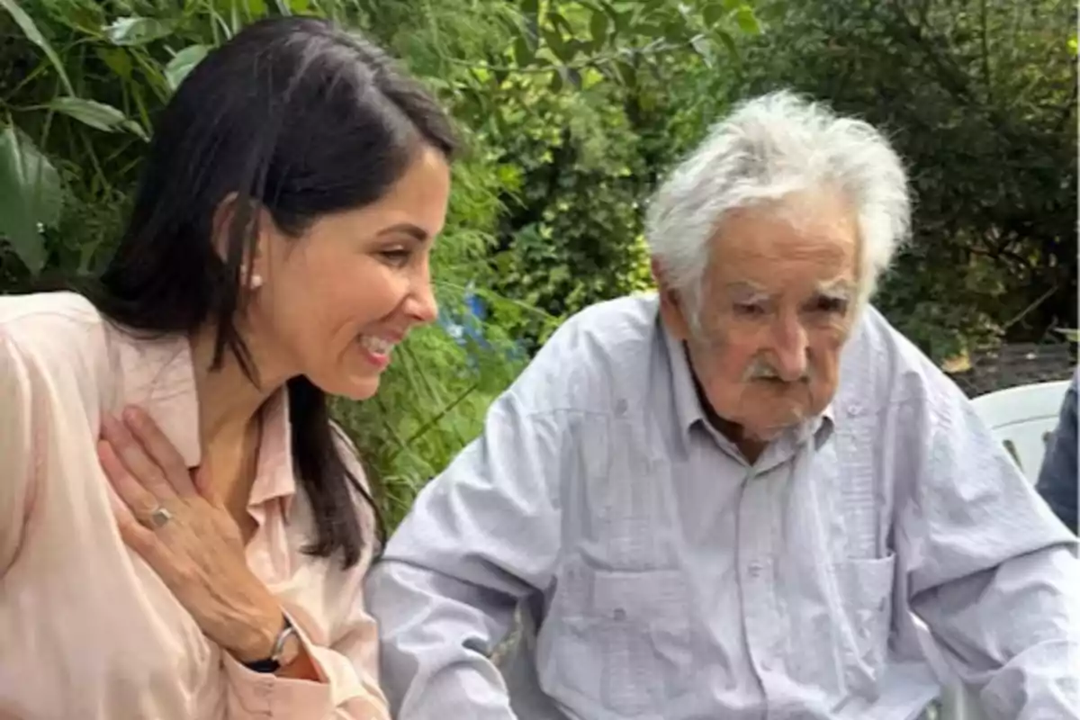 Una mujer sonriente y un hombre mayor están sentados juntos al aire libre rodeados de vegetación.