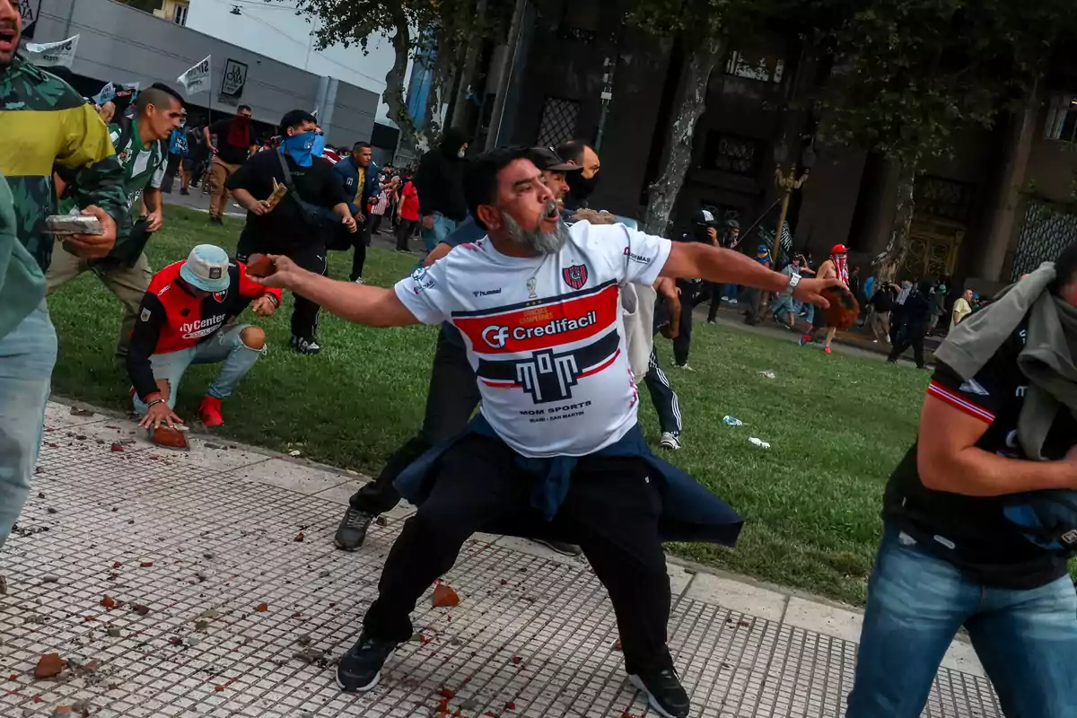 A group of people is participating in a demonstration in a public space, some of them appear to be throwing objects.