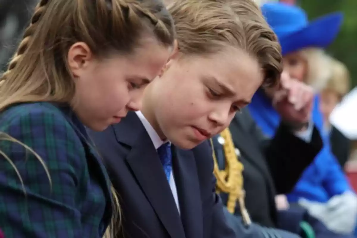 Dos niños con expresión seria, uno con trenza y otro con traje, en un evento formal. Dos niños con expresión seria, uno con trenza y otro con traje, en un evento formal.