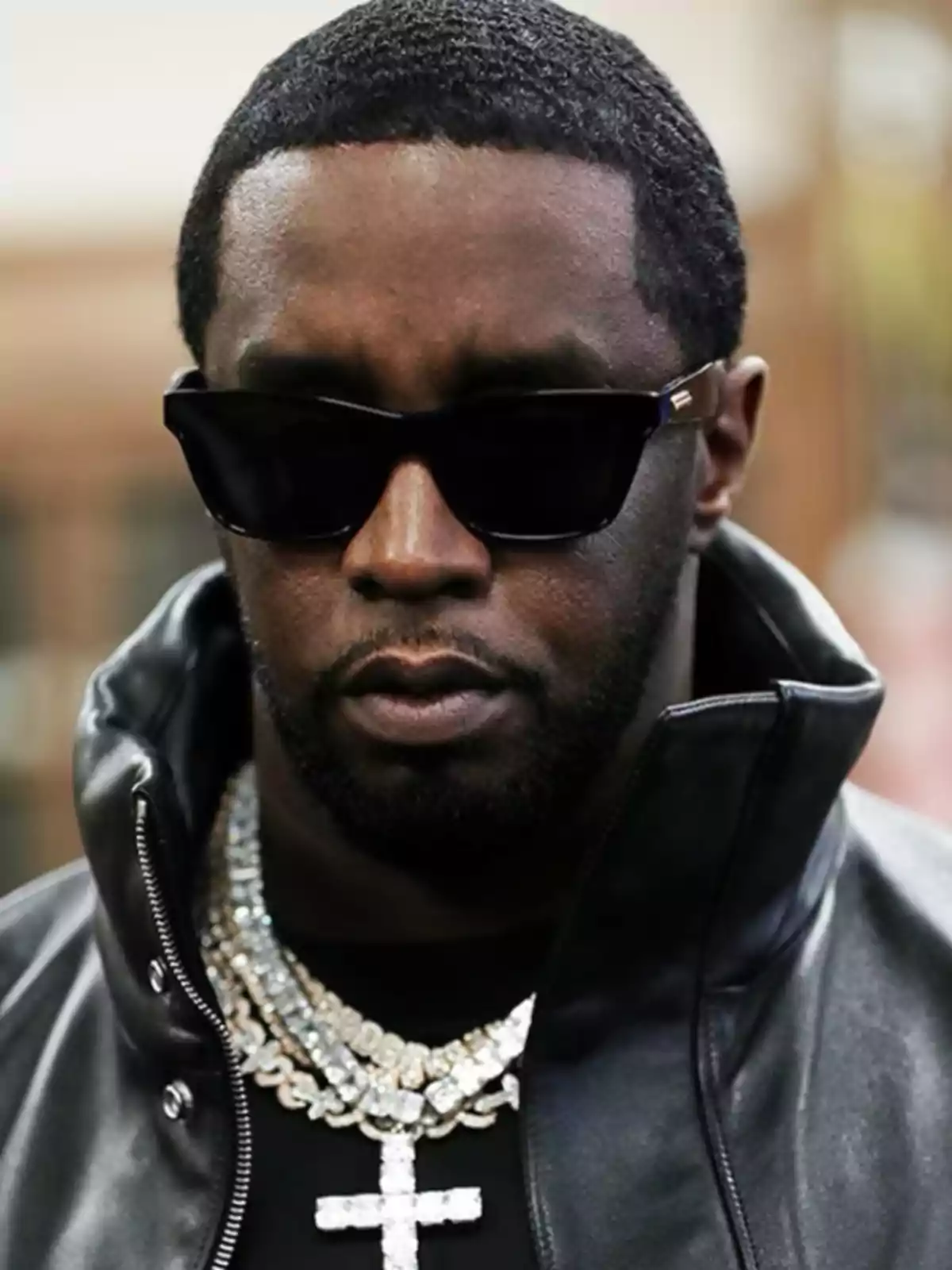 Man with sunglasses and a leather jacket, wearing shiny necklaces.