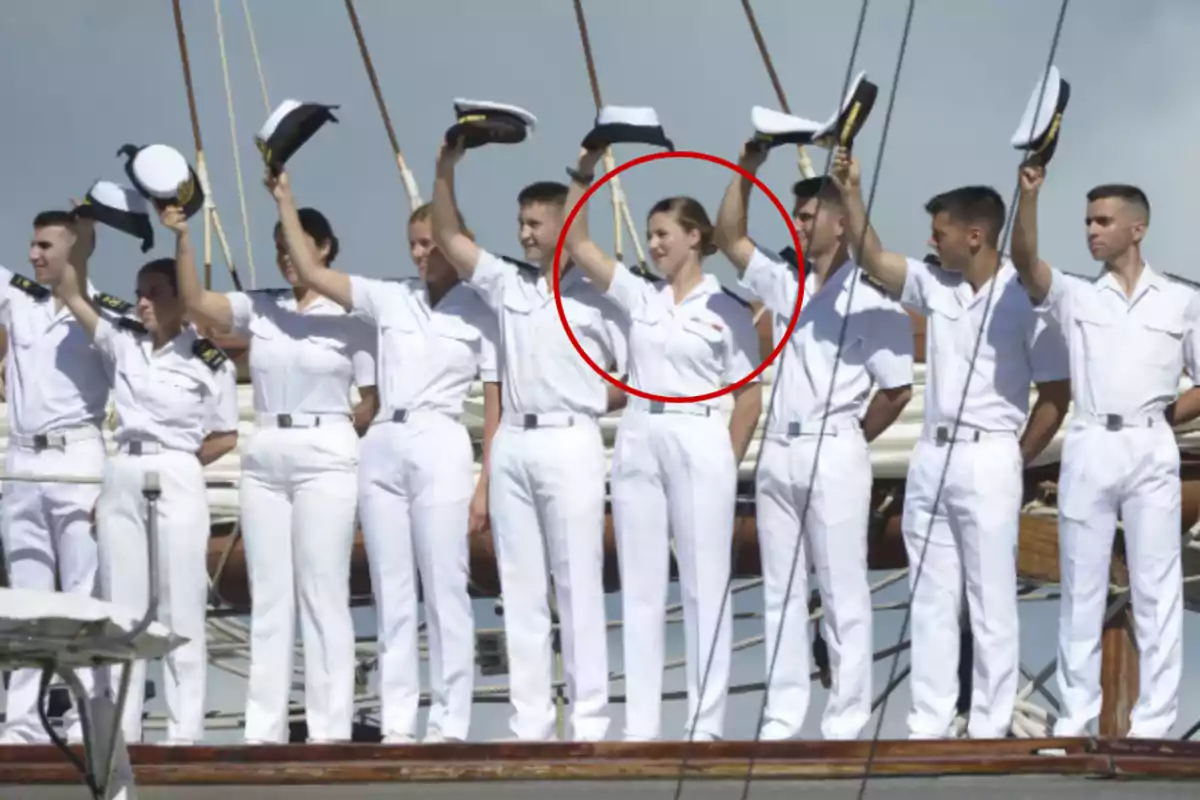 Un grupo de personas en uniforme naval blanco levantando sus gorras en un barco.