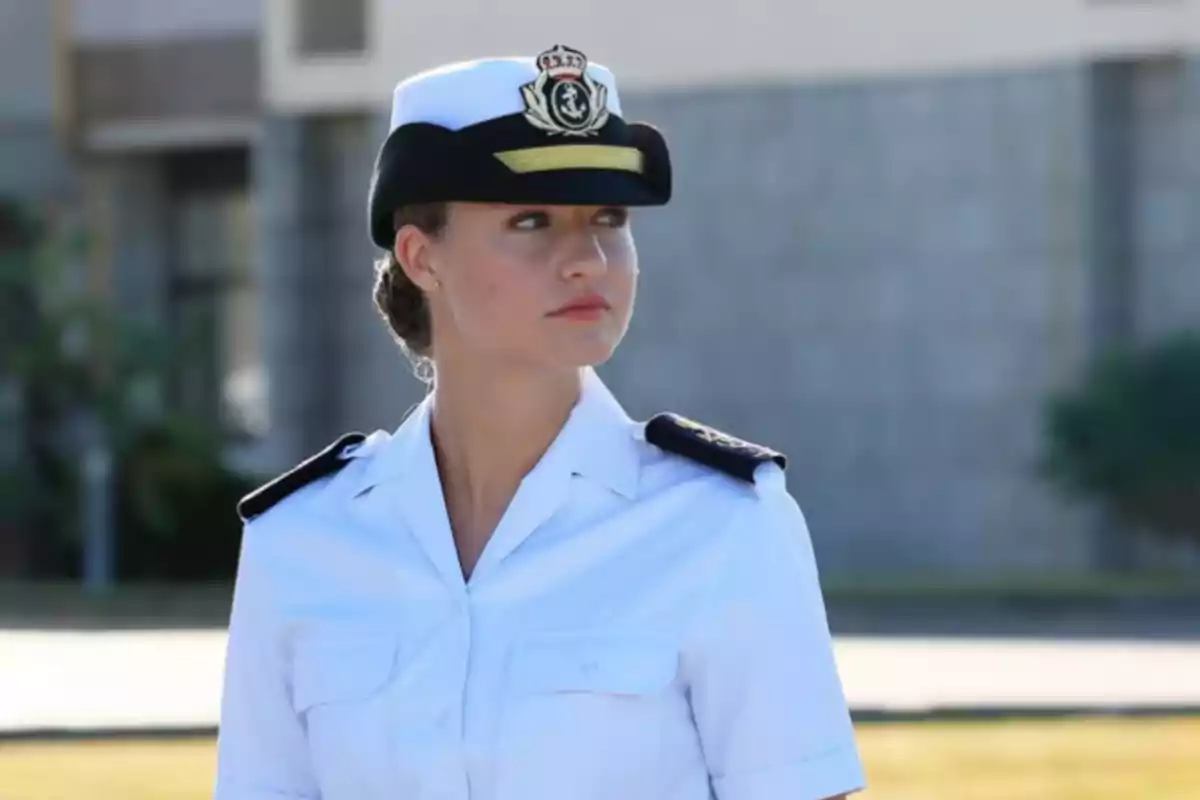Una persona con uniforme naval blanco y gorra negra está de pie al aire libre.