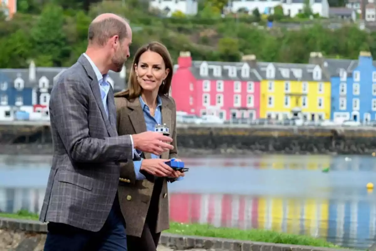 Two people walking and talking by a lake with colorful houses in the background. Two people walking and talking by a lake with colorful houses in the background.