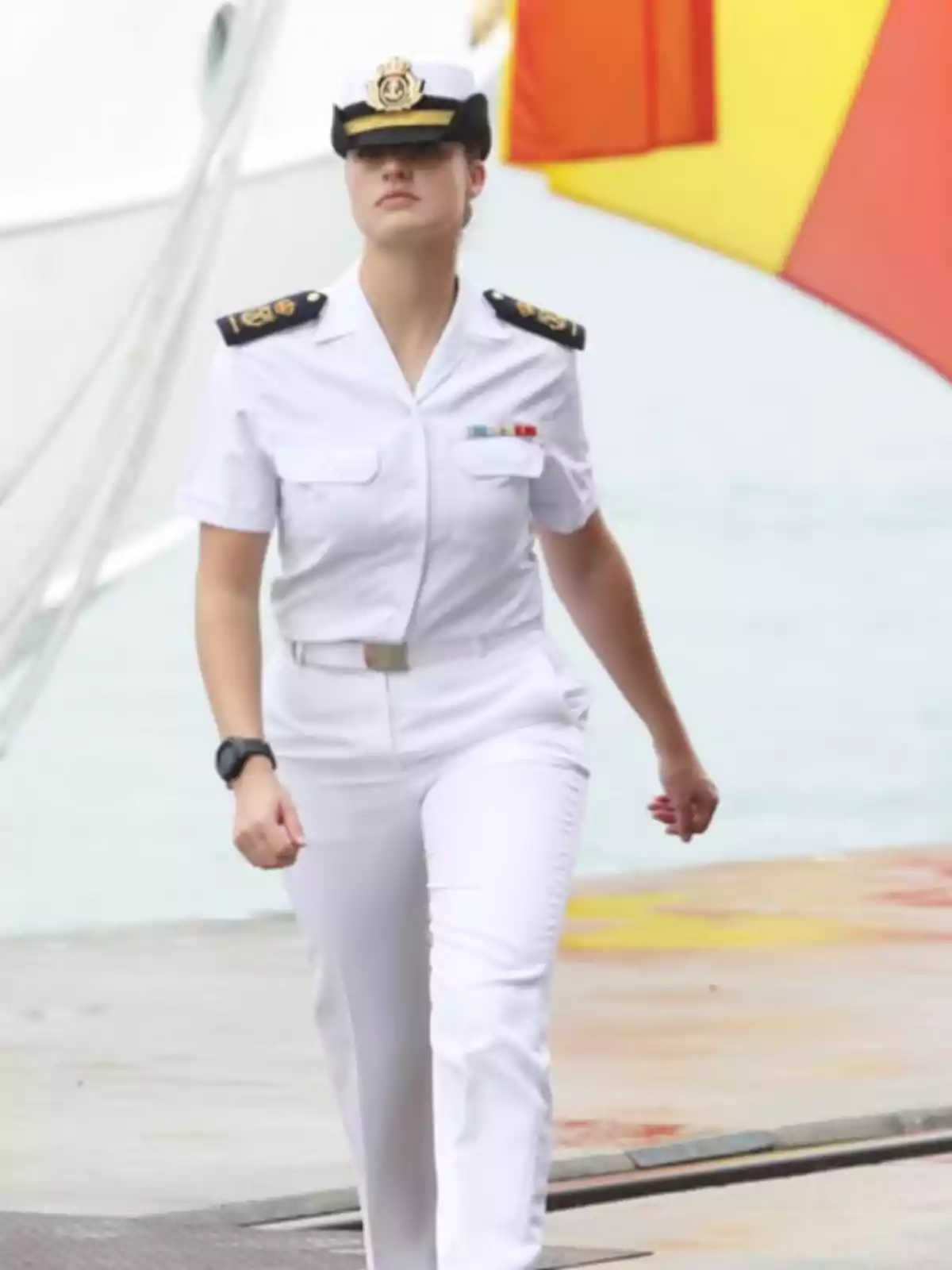 Mujer con uniforme naval blanco caminando cerca de un barco con una bandera de fondo. Mujer con uniforme naval blanco caminando cerca de un barco con una bandera de fondo.