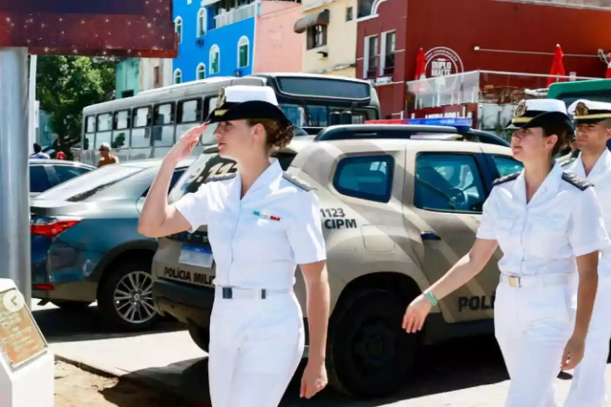 Personas en uniforme militar blanco caminando por una calle con vehículos y edificios coloridos de fondo.