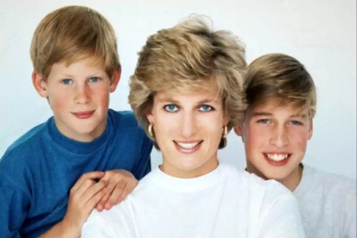 Una mujer rubia sonriente con dos niños rubios a su lado, todos con camisetas claras y fondo blanco.