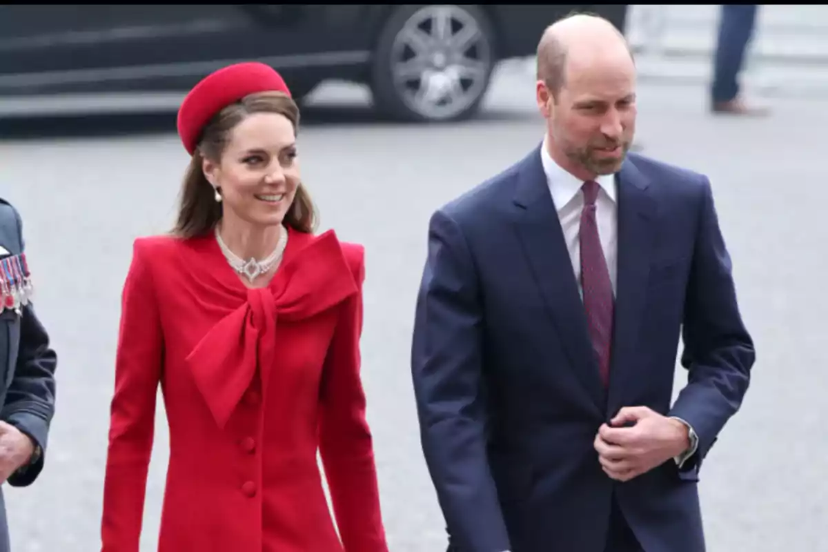 A woman in an elegant red outfit and a man in a blue suit walk together at a formal event.