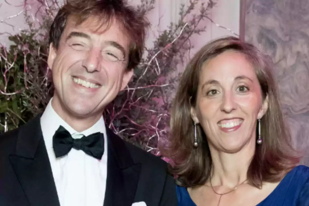 Una pareja sonriente vestida de gala en un evento elegante con un fondo decorativo.