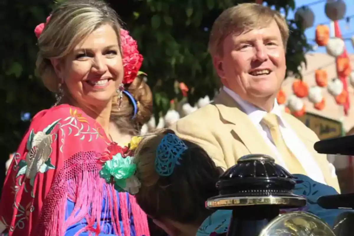 Una pareja sonriente vestida con trajes tradicionales, rodeada de decoraciones festivas al aire libre.