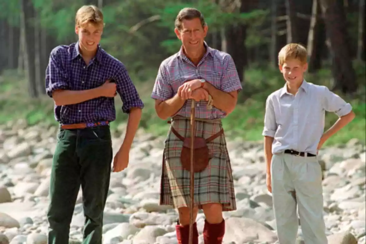 Three people standing on rocky ground in a wooded setting, two of them wearing plaid jerseys and one wearing a kilt.