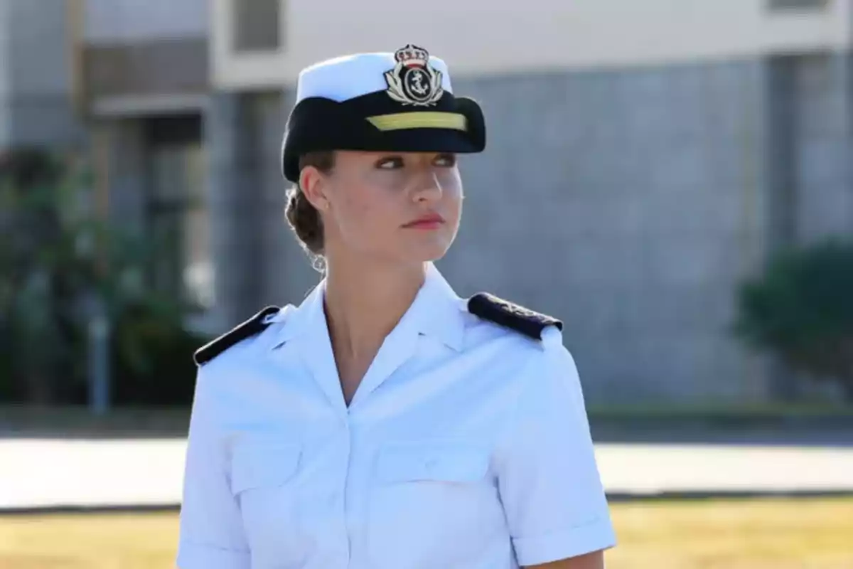 Mujer joven con uniforme blanco de marina y gorra mirando hacia un lado en un entorno exterior