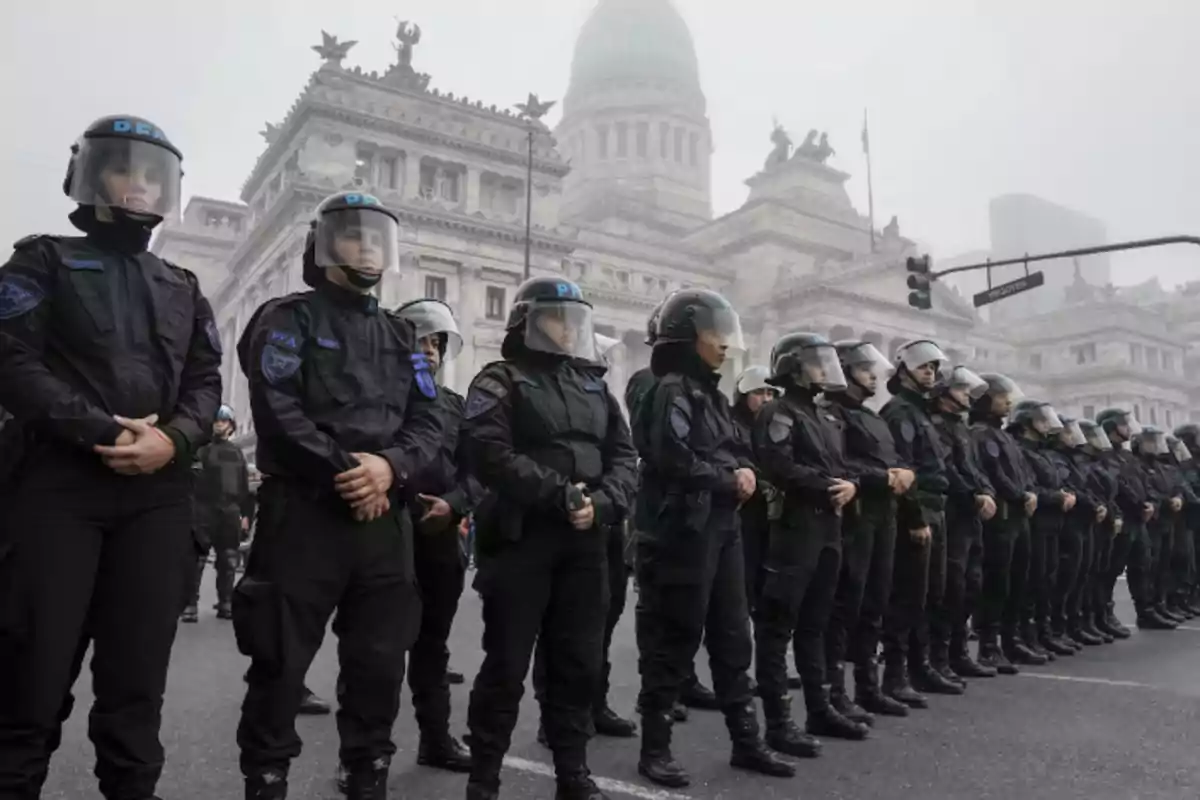 Un grupo de policías con equipo antidisturbios forma una línea frente a un edificio histórico. Un grupo de policías con equipo antidisturbios forma una línea frente a un edificio histórico.