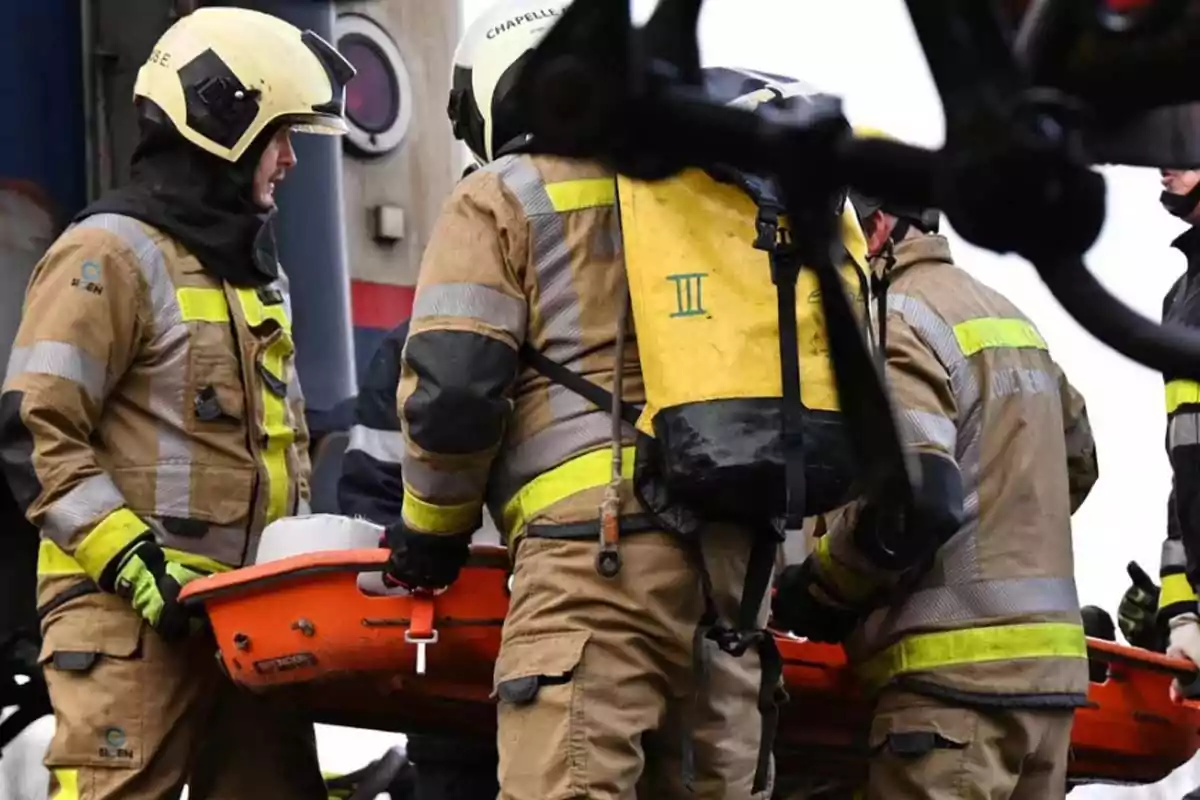 Firefighters wearing protective gear carry an orange stretcher during a rescue operation. Firefighters wearing protective gear carry an orange stretcher during a rescue operation.