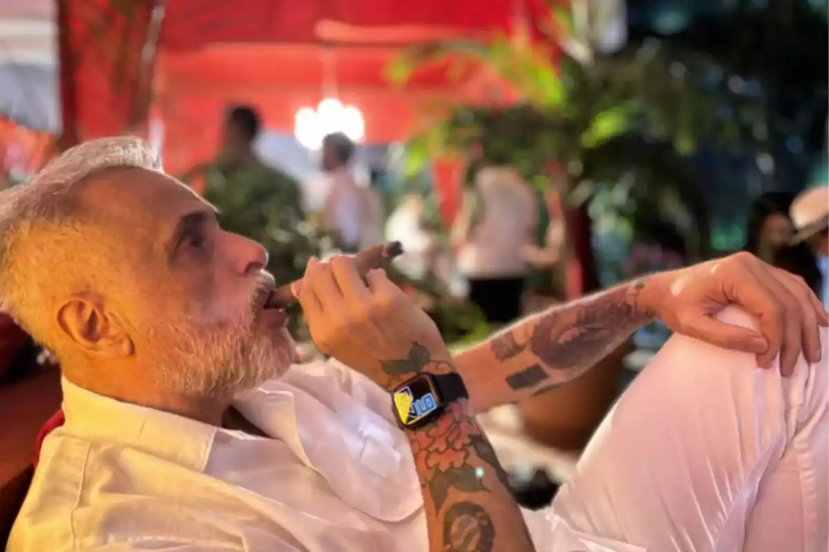 Man with a beard and tattoos enjoying a cigar in a relaxed and colorful setting.