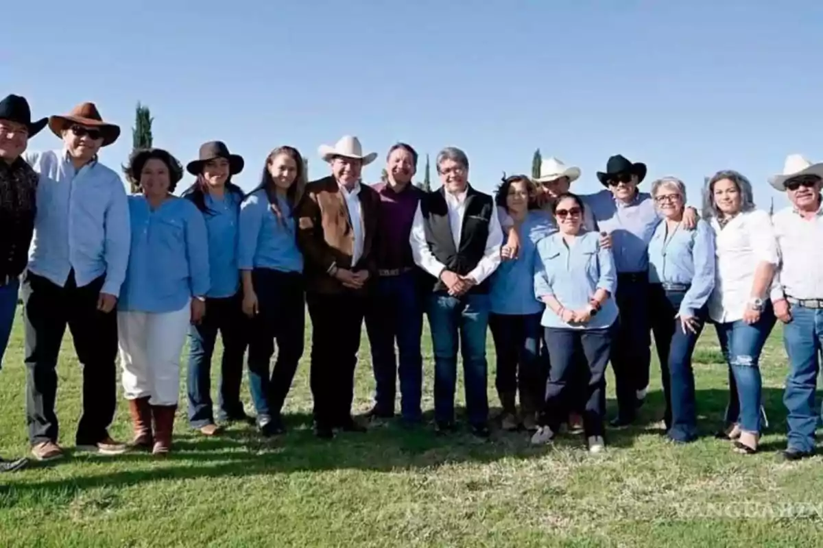 Grupo de personas posando al aire libre en un campo, la mayoría lleva sombrero y ropa casual, con cielo despejado de fondo