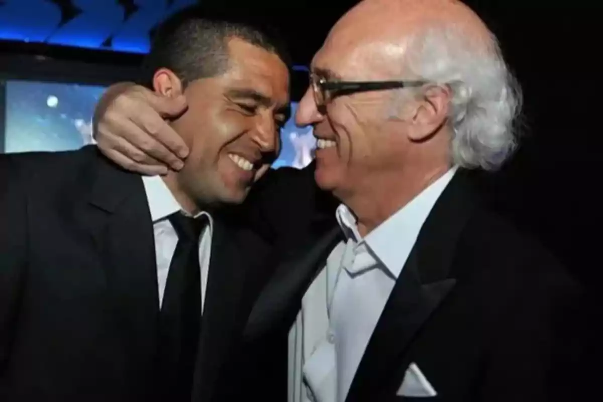 Two men smile and embrace affectionately, both wearing formal suits. Two men smile and embrace affectionately, both wearing formal suits.