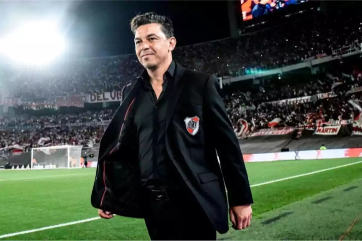 Un hombre con traje negro camina por un estadio lleno de espectadores.