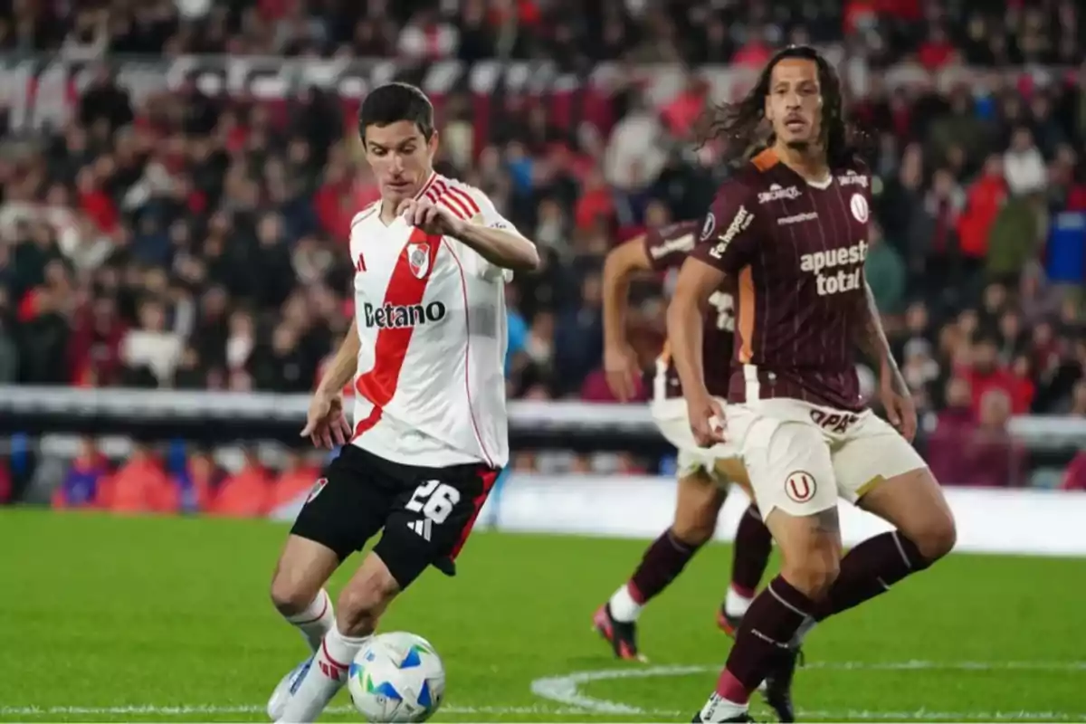 River Plate player controls the ball while a Universitario player watches during a soccer match in a stadium full of spectators. River Plate player controls the ball while a Universitario player watches during a soccer match in a stadium full of spectators.