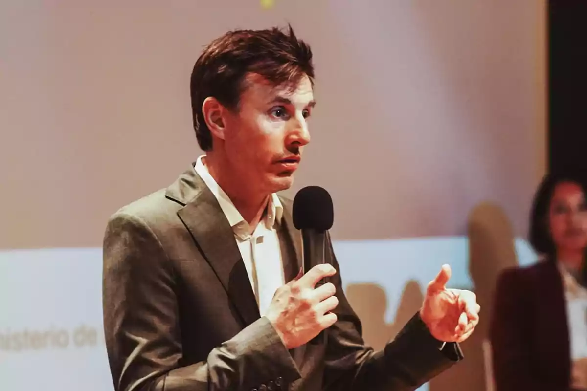 Un hombre en traje hablando con un micrófono en la mano durante una presentación.