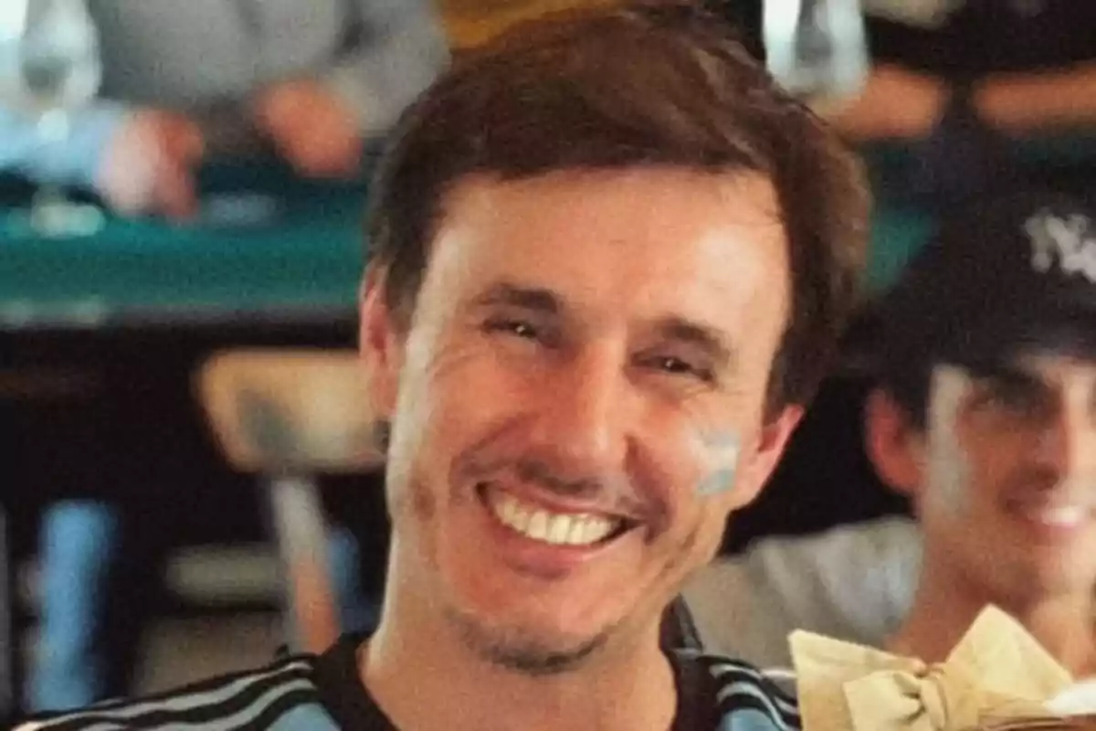Hombre sonriente con camiseta celeste y negra en un ambiente social