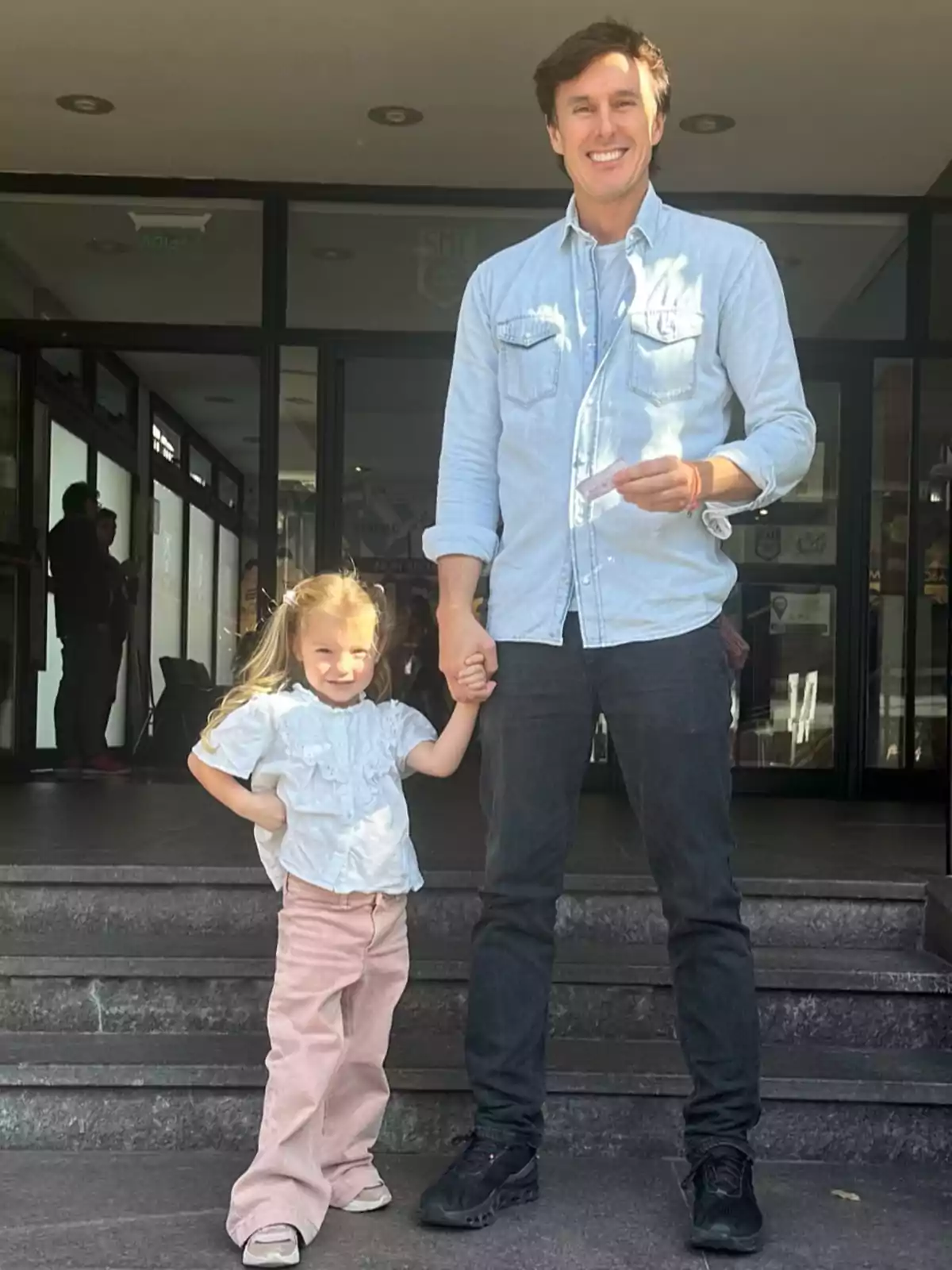 A man and a girl smile as they pose holding hands at the entrance of a building. A man and a girl smile as they pose holding hands at the entrance of a building.