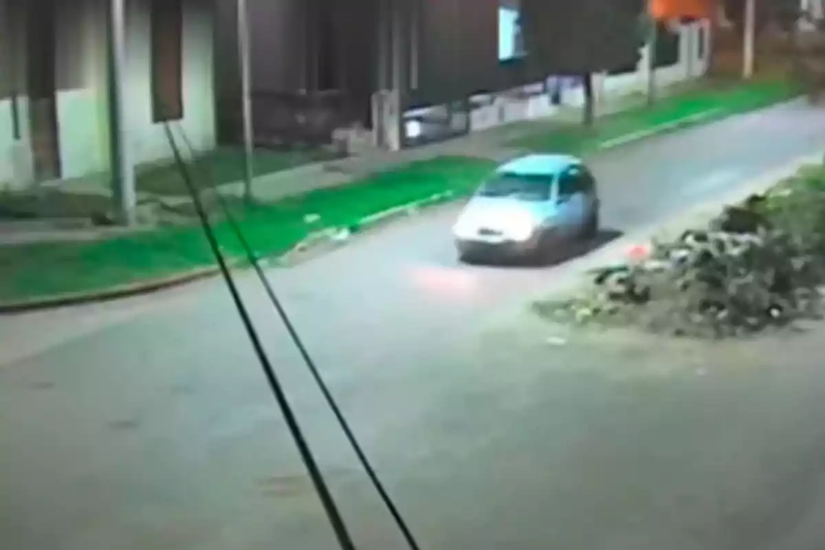 A car drives down a residential street at night, captured by a security camera.