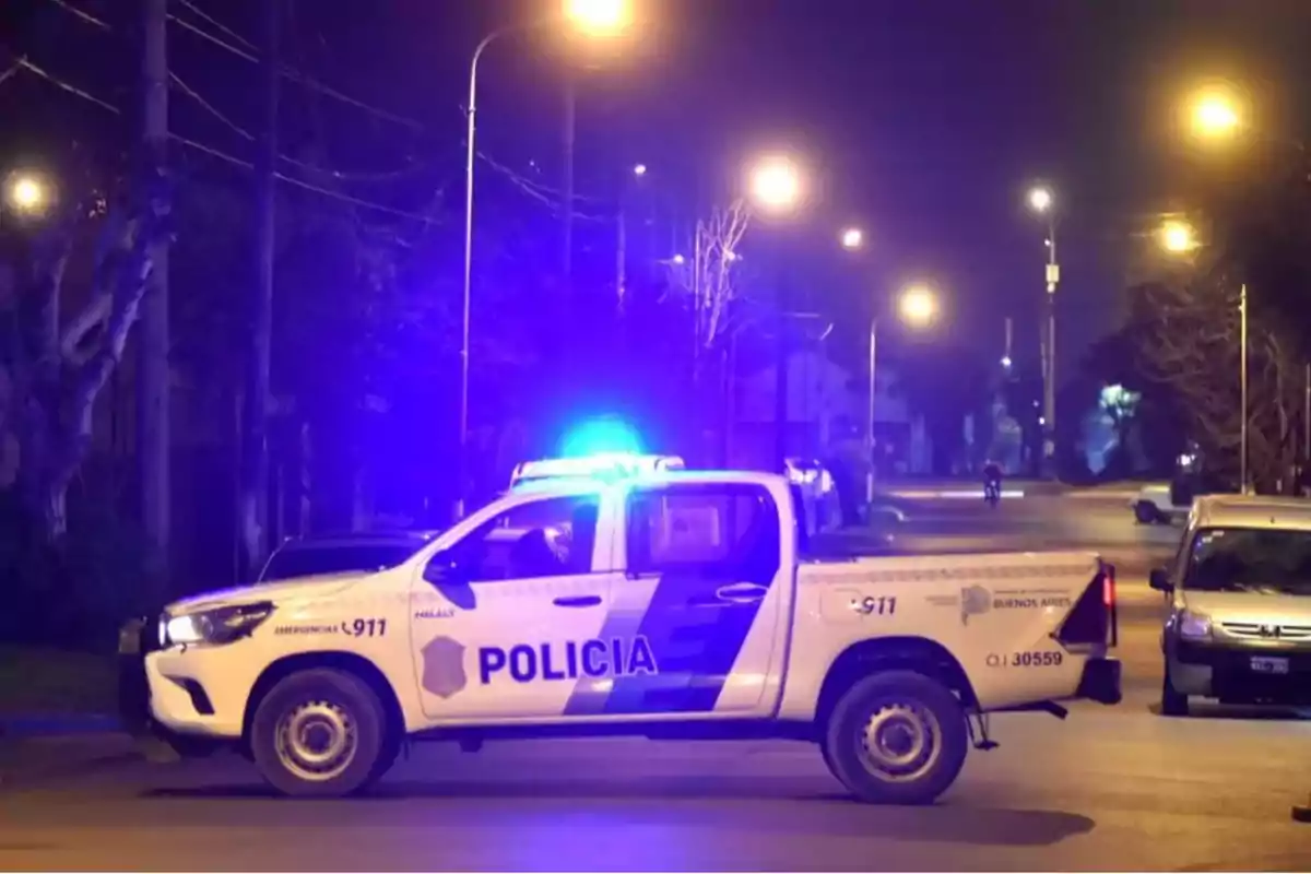 A police van with blue lights on is parked on a street lit by streetlights at night.